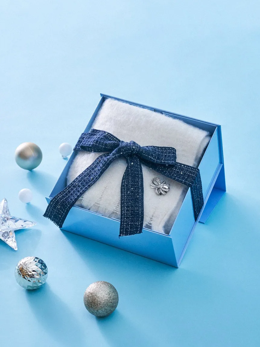 青いギフトボックスに入った白い毛布。ボックスには青いリボンとブローチが飾られ、周りにはクリスマスオーナメントが散りばめられています。