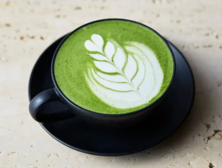 抹茶ラテが黒いカップとソーサーに入っており、表面に葉っぱのラテアートが施されている
