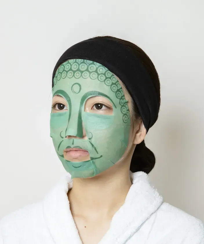 仏陀の顔が描かれたフェイスマスクを着用した女性のクローズアップ。