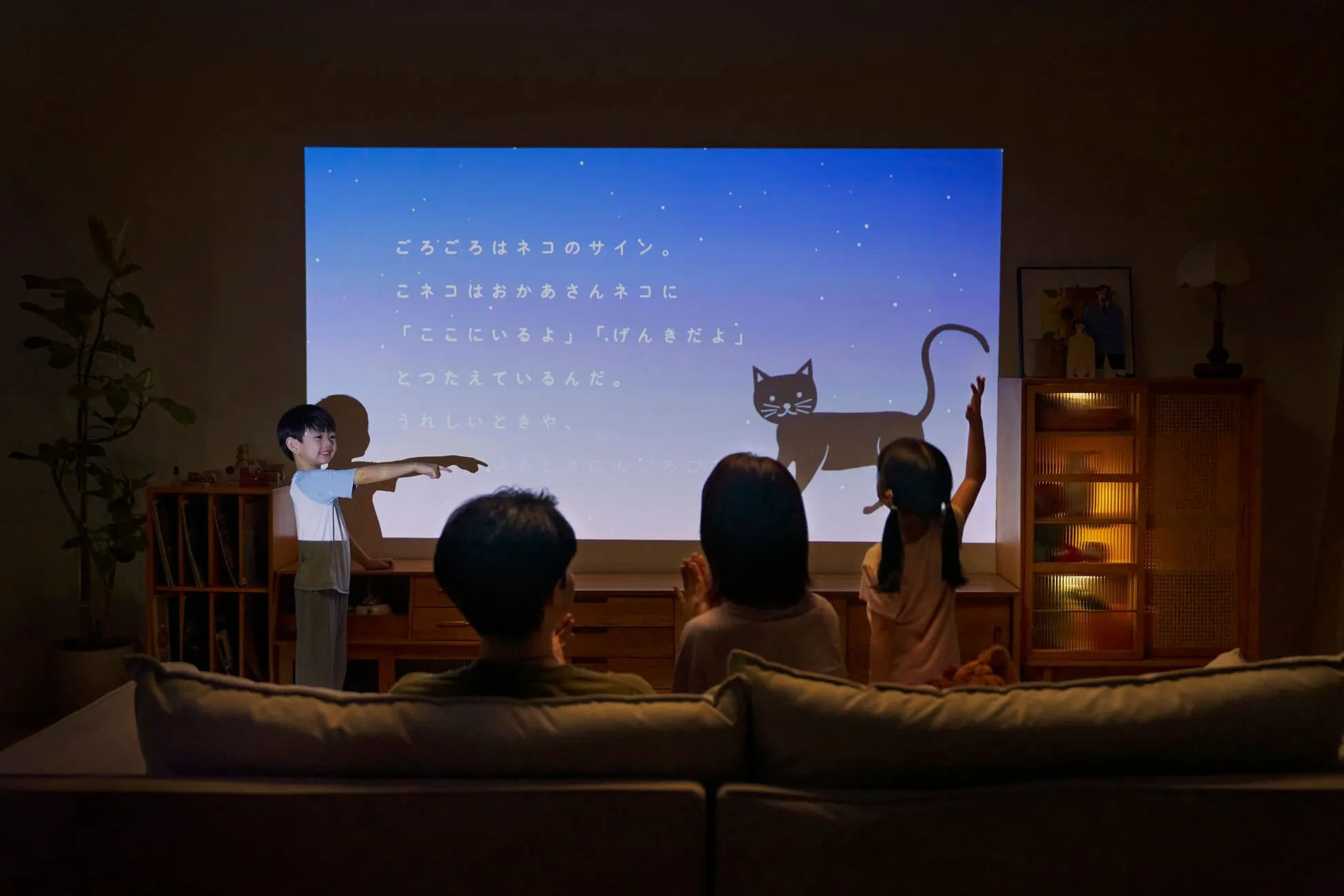 プロジェクターで絵本のような映像を見ている家族の様子。子供たちが映像に合わせて楽しそうにしている。