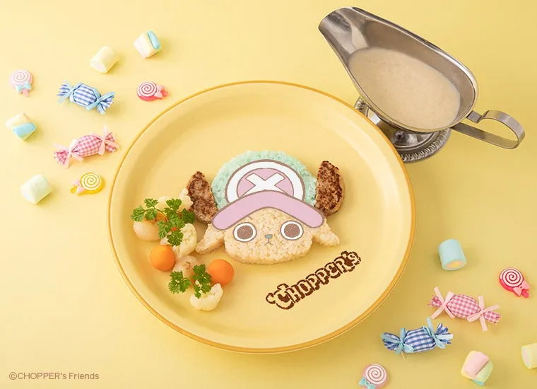 チョッパーの顔を模したお子様ランチ。黄色い皿に、チョッパーの顔型のご飯、ハンバーグ、野菜、ソースが添えられ、周りにはキャンディーが散りばめられています。