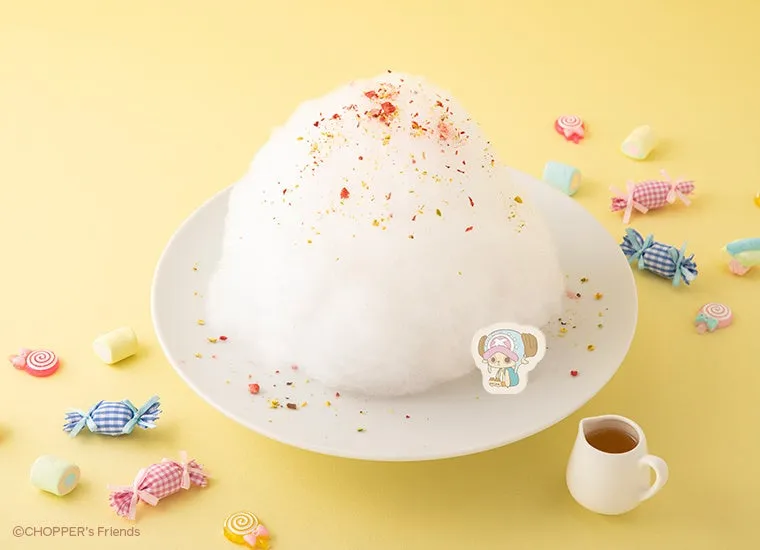 白い綿菓子が皿に盛られており、周りにキャンディやマシュマロが散りばめられた写真です。綿菓子の上にはトッピングが施され、チョッパーのキャラクターのステッカーが添えられています。手前にはシロップが入った小さなピッチャーが置かれています。