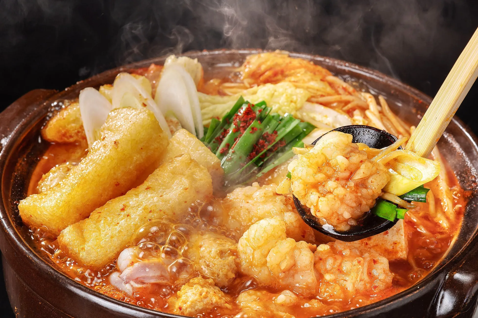 熱々の鍋料理の写真。具材には、揚げ豆腐、ネギ、ニラ、もつなどが入っており、湯気が立っている様子が食欲をそそる。