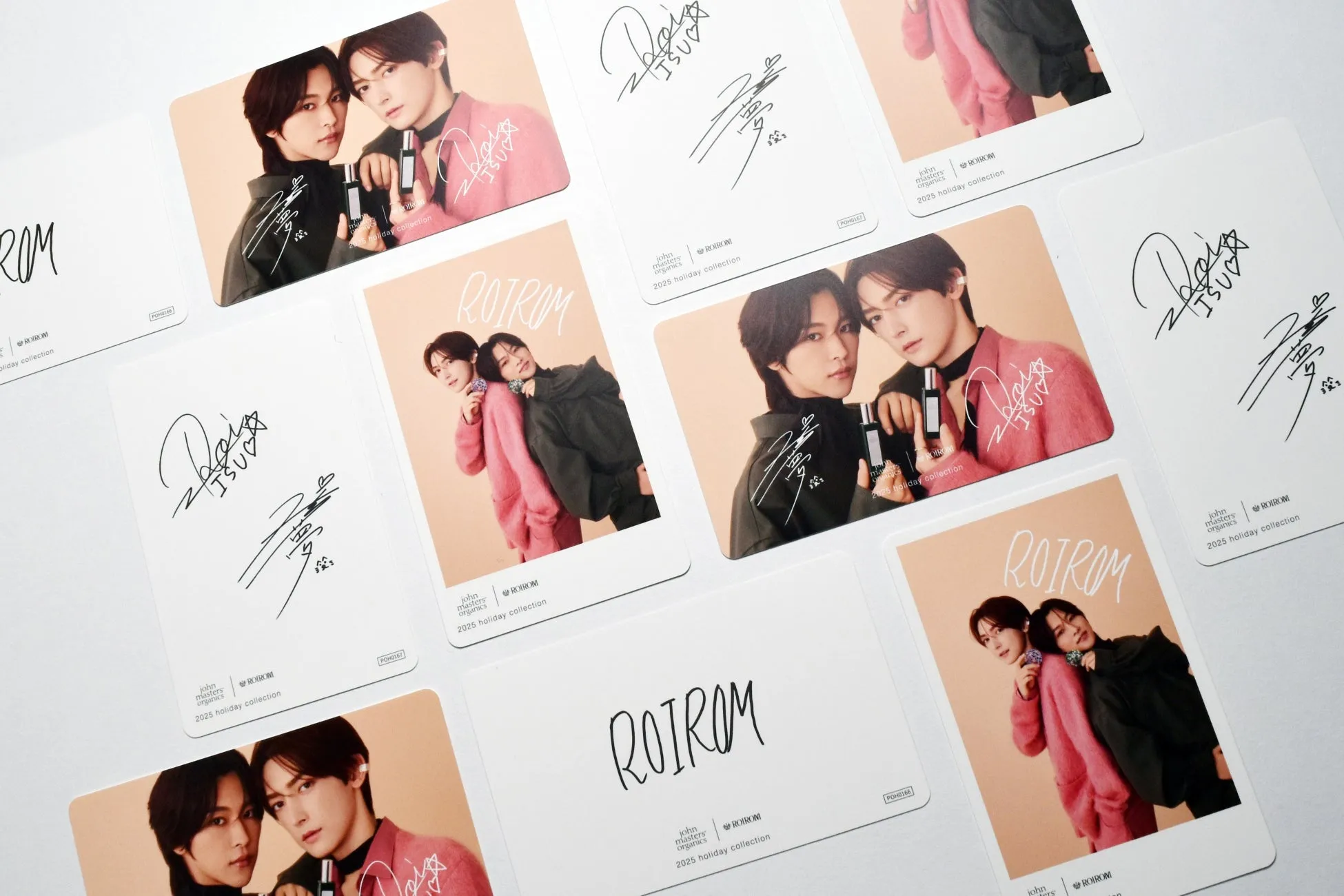 2人の男性が写った複数のカード。カードにはサインやブランドロゴ、商品名が記載されている。カードは白を基調とし、男性2人の写真がメインで、ピンク色と黒色の服を着ている。