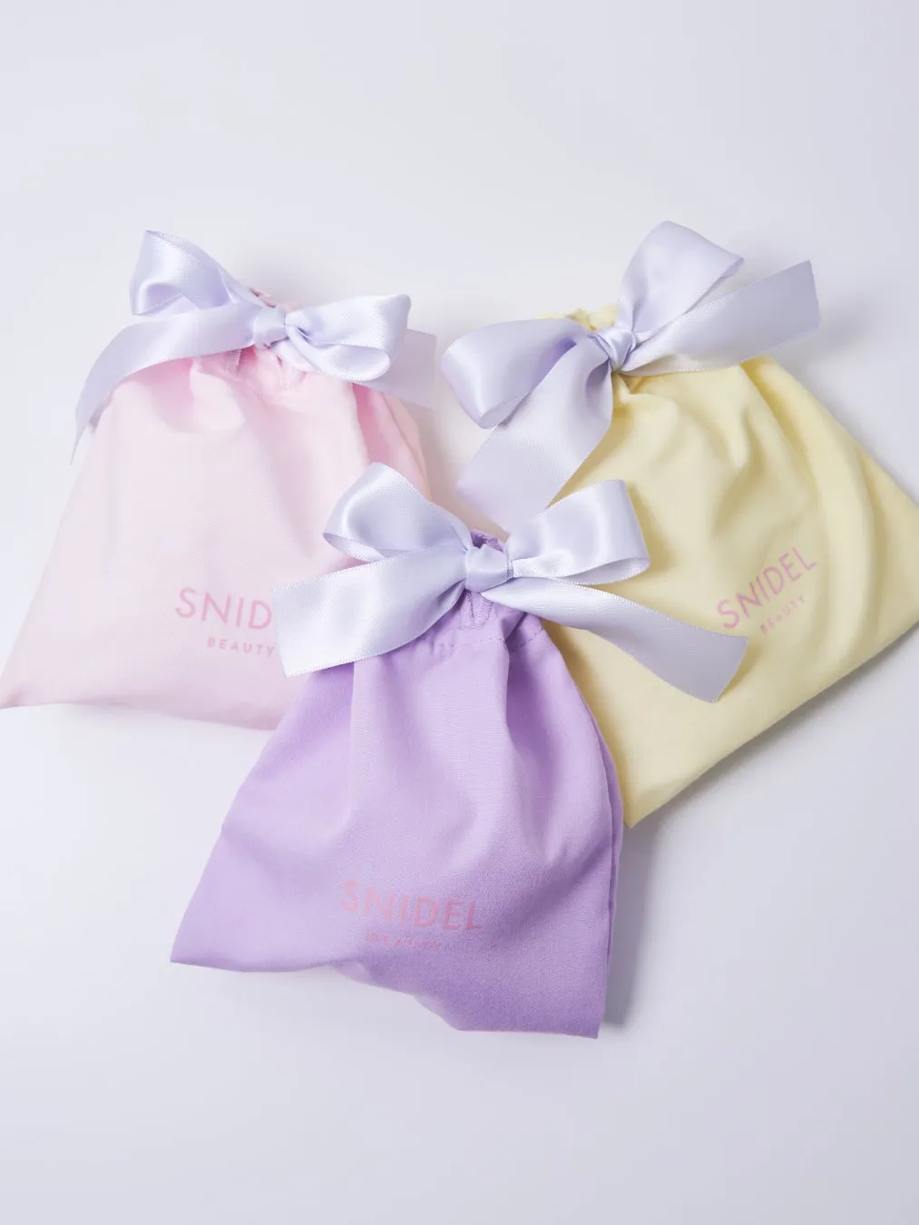 ピンク、薄紫、黄色の巾着袋が3つ並んだ写真。それぞれ白いリボンで結ばれており、SNIDEL BEAUTYのロゴが見える。
