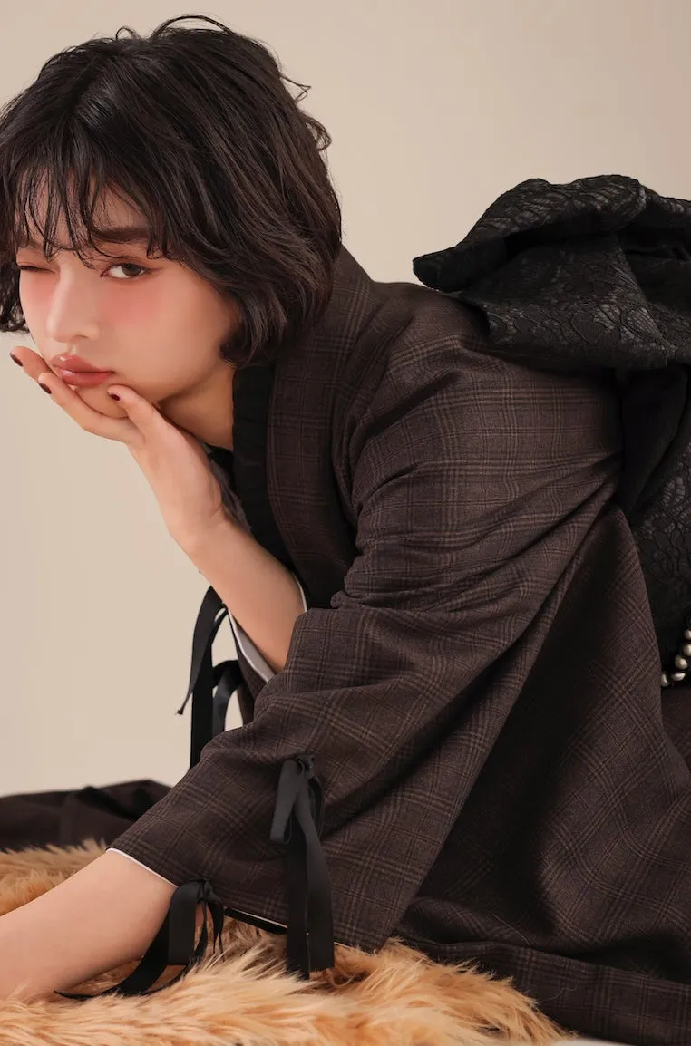 女性がポーズをとっている写真。彼女は茶色のチェックのジャケットを着ており、顔にはチークが塗られている。彼女はウィンクをしており、手で顔を支えている。