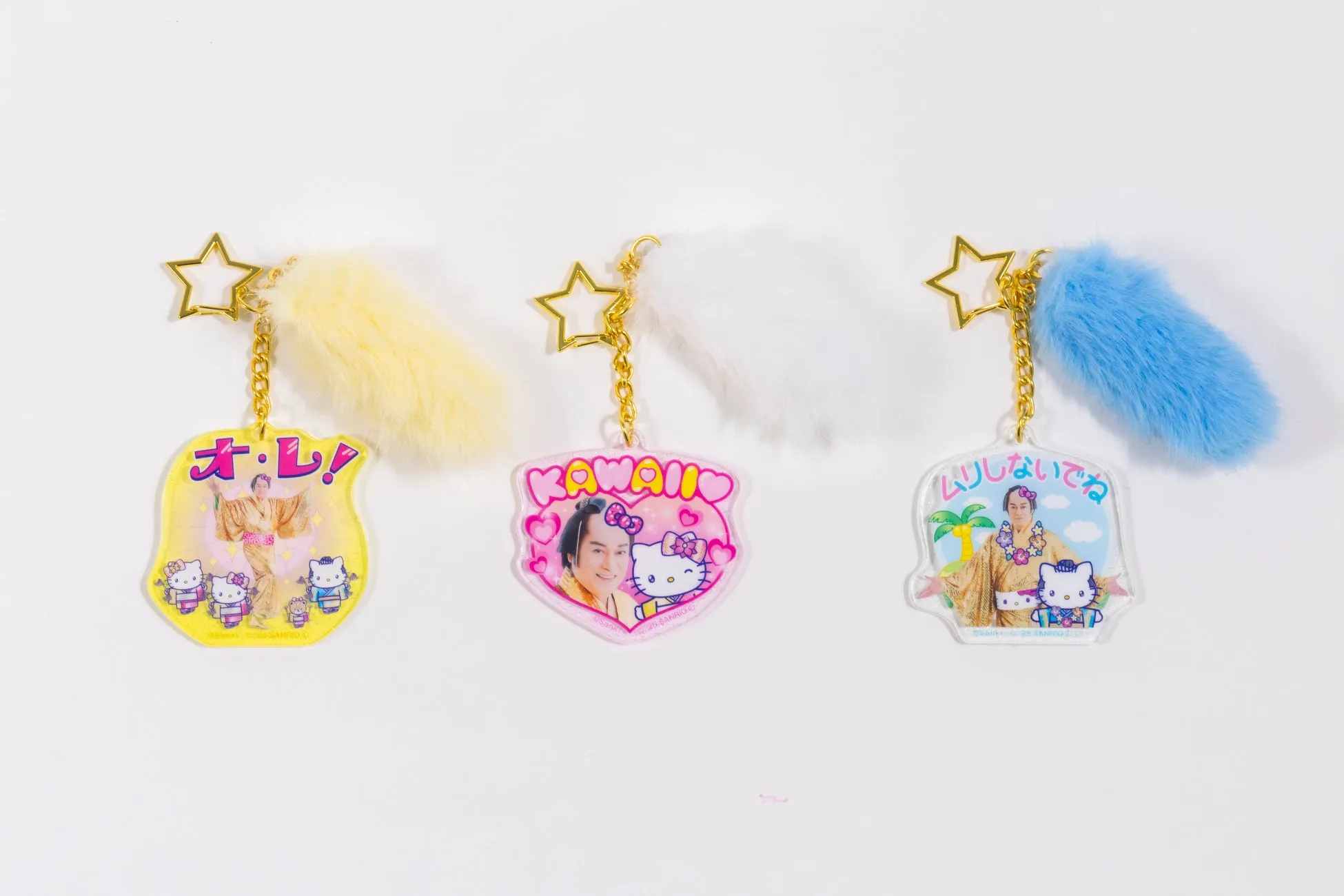 3つのキーホルダーが写っている写真。キーホルダーには、キャラクターと日本語のテキストが印刷されており、それぞれ異なる色の毛玉が付いている。