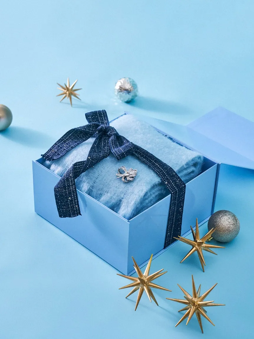 青いギフトボックスに入った、水色の毛布とリボン、ブローチ、星のオーナメントが置かれた、クリスマスをテーマにした写真です。