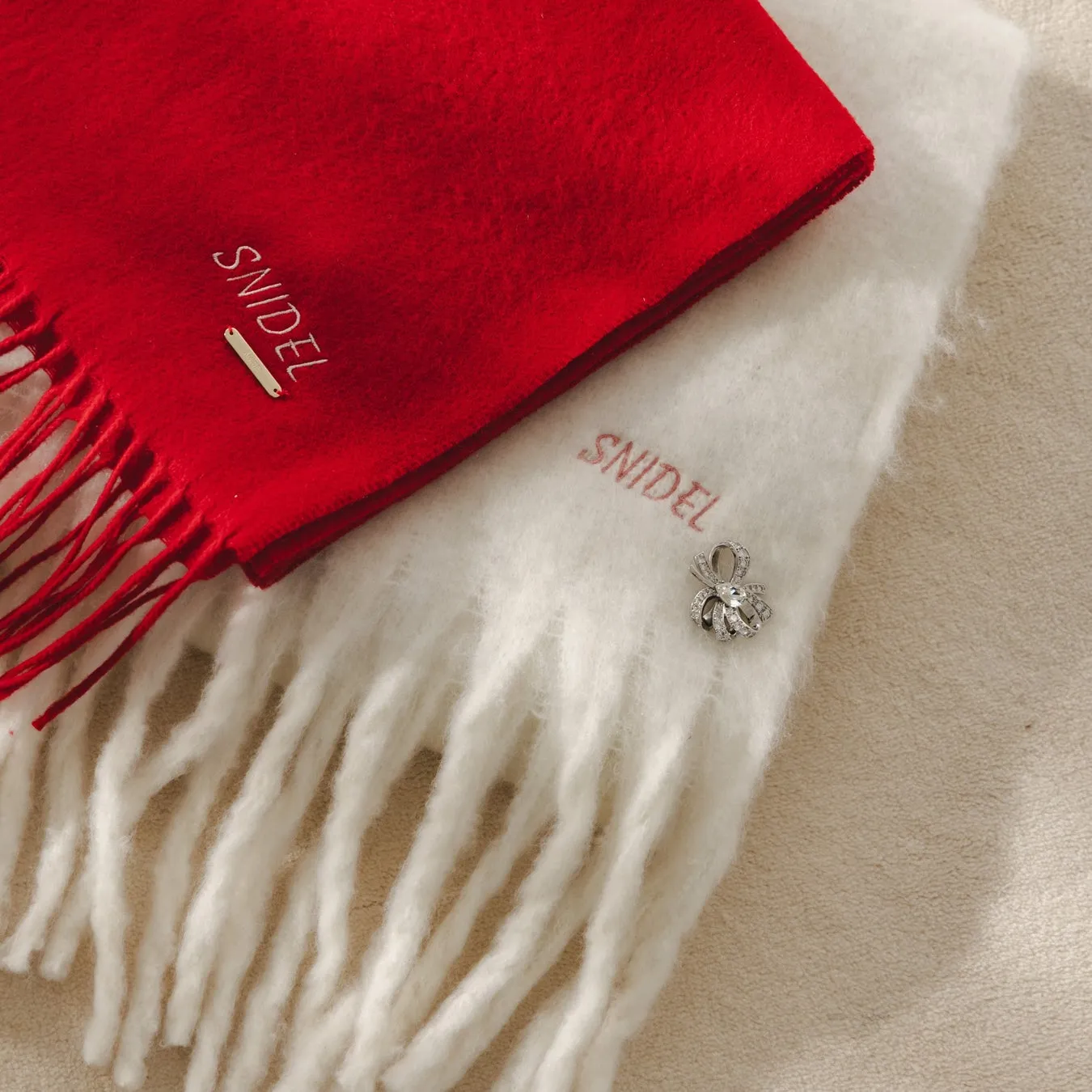 赤と白の2色のスカーフの写真。両方のスカーフに「SNIDEL」のロゴが入っており、白いスカーフには装飾的なブローチが付いている。