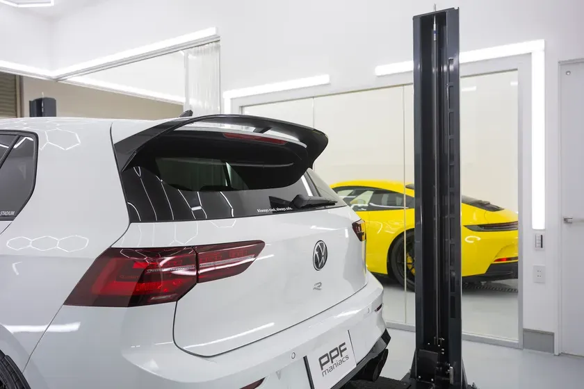 白いフォルクスワーゲンRの車の後ろ姿と、背景に黄色いポルシェ911が見える写真