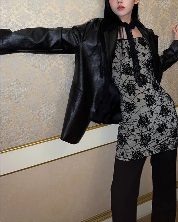 女性が黒いジャケットと、花柄のミニドレス、黒いパンツを着用してポーズをとっている写真です。