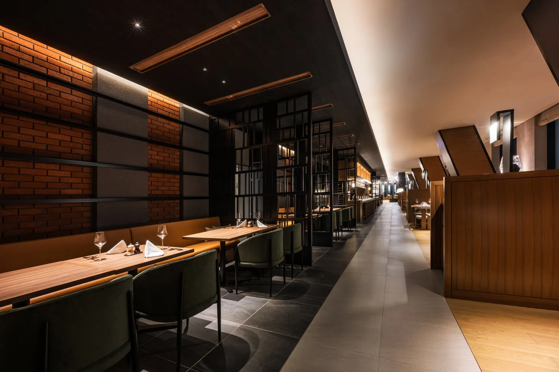 レストランのインテリアの写真。レンガの壁、木製のテーブルと椅子、そして長い通路がある。