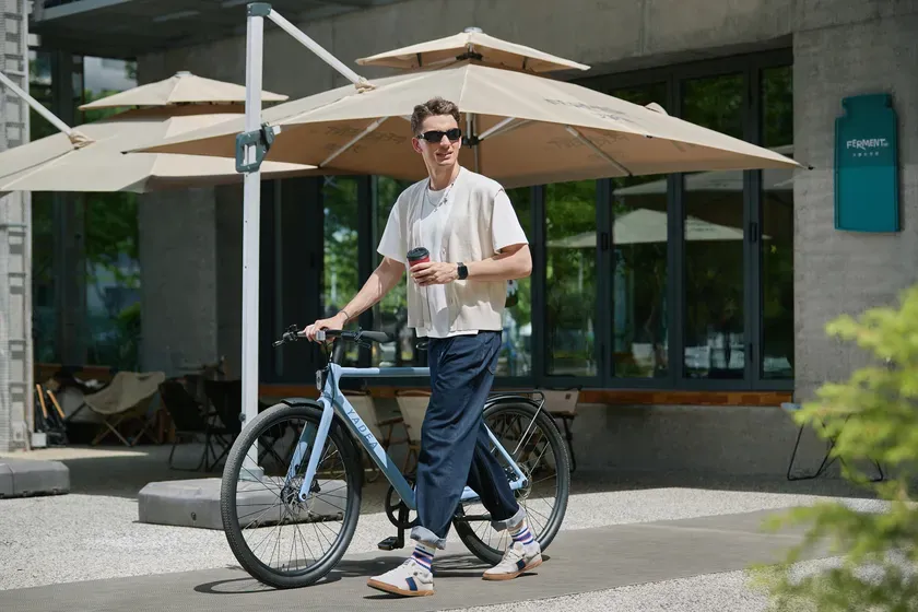 男性が電動アシスト自転車を押しながら街を歩いている様子