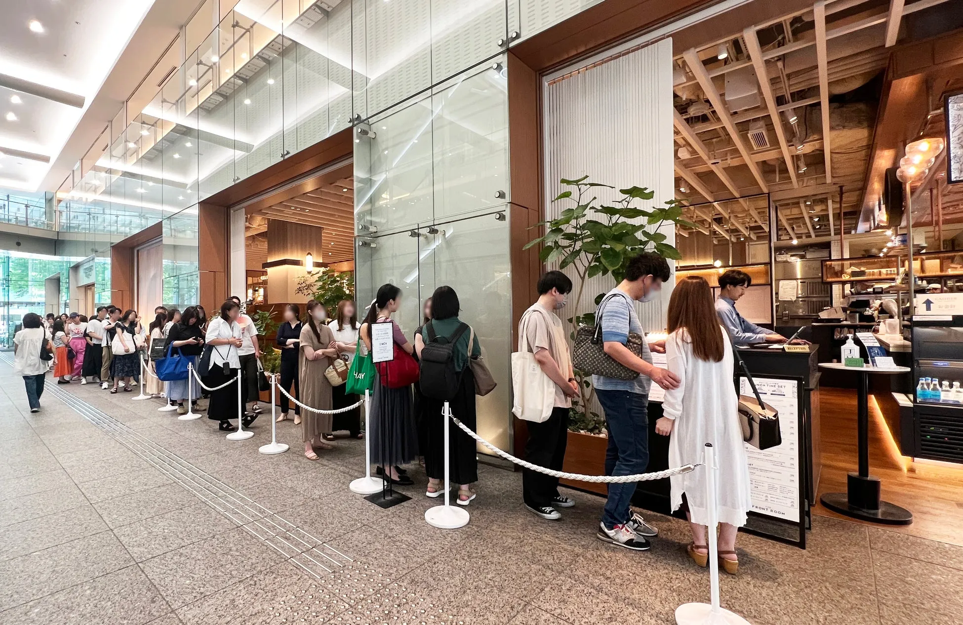 カフェの入り口で並んでいる人々の写真。列ができており、多くの人が待っている様子が写っています。カフェの看板にはメニューが表示されています。