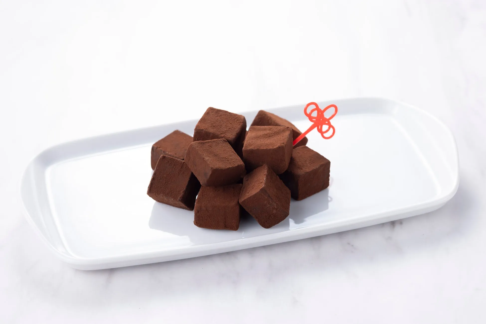 白い皿に盛られた、チョコレートの立方体と赤いピックの画像。