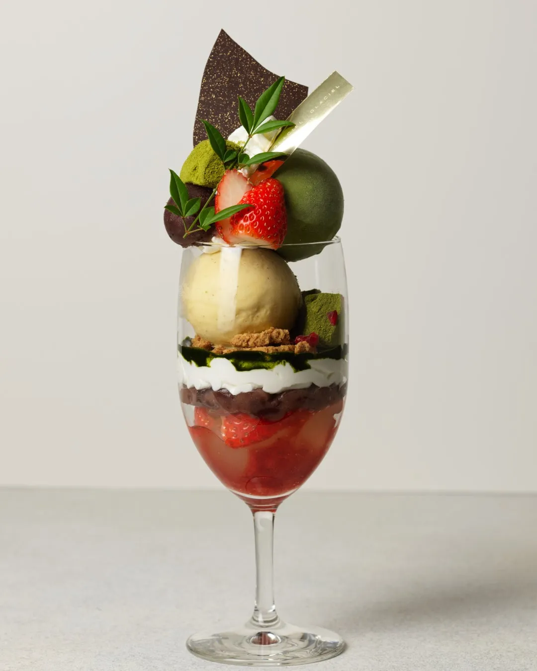 グラスに入ったパフェ。イチゴや抹茶のアイス、チョコレートなどがトッピングされている。