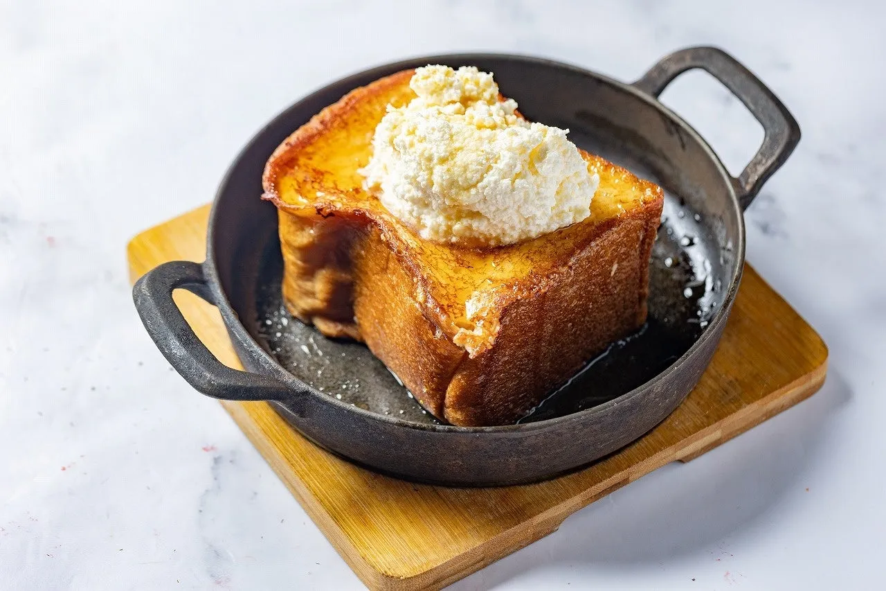 熱々のフレンチトーストが、鉄鍋に入って木製のボードの上に置かれている。フレンチトーストの上にはクリームがたっぷり。