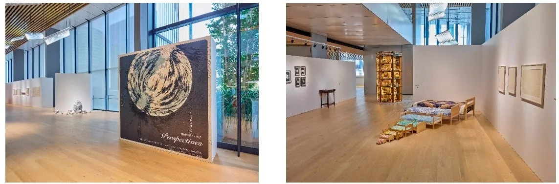 美術館の展示の様子を捉えた写真。大きな絵画が展示されており、その奥には、小さなベッドが階段状に並べられたインスタレーション作品が見える。