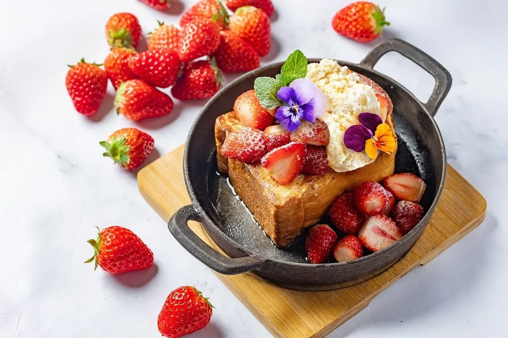 いちごがたっぷりトッピングされた、おしゃれなフレンチトーストの写真です。鉄鍋に入っていて、お花も添えられています。