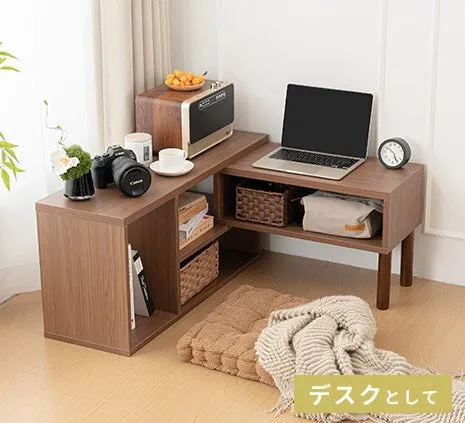 木製のL字型デスク。ノートパソコン、カメラ、書籍、バスケット、時計などが置かれている。床にはクッションと毛布が置かれている。