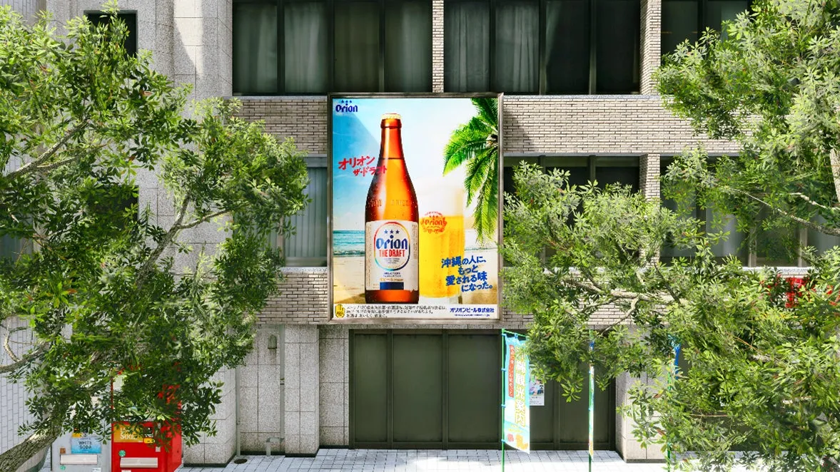 ビルの壁に貼られたオリオンビールの広告。広告には、ビール瓶とグラス、ビーチの風景が描かれています。周囲には木々が生い茂り、建物の窓が見えます。