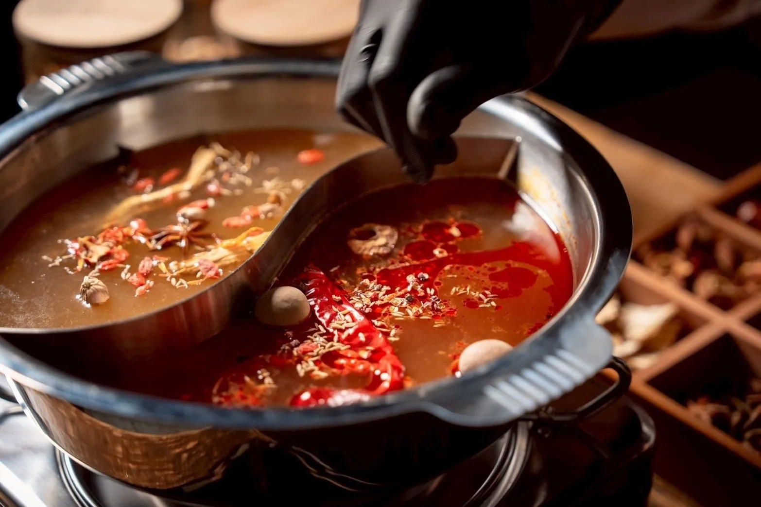 二色のスープが入った鍋に、黒い手袋をした人が調味料を入れている様子