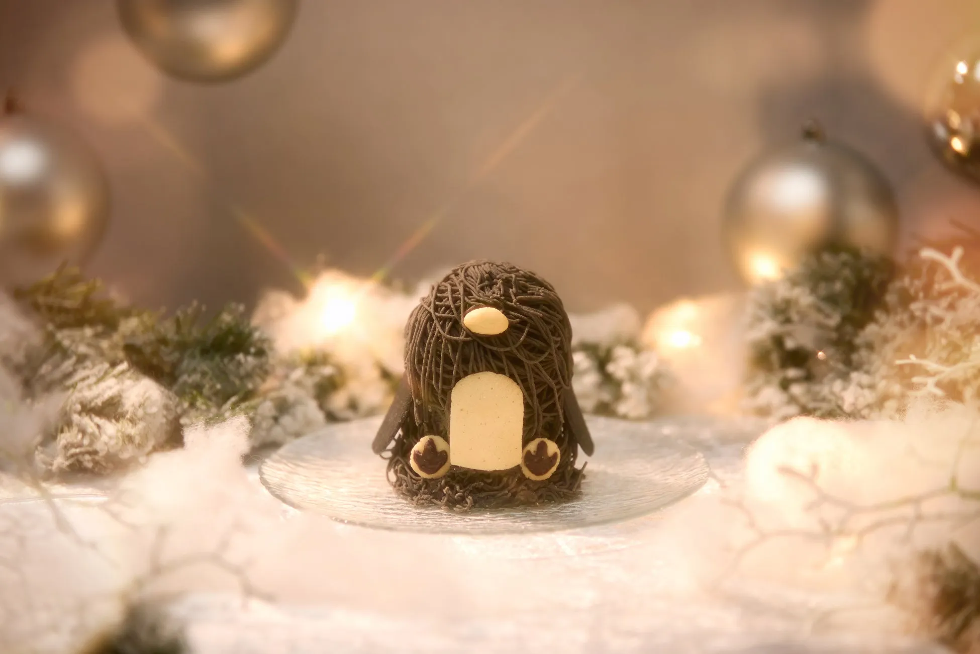 ペンギンの形をしたケーキが、クリスマスをテーマにした装飾の中に置かれている写真。