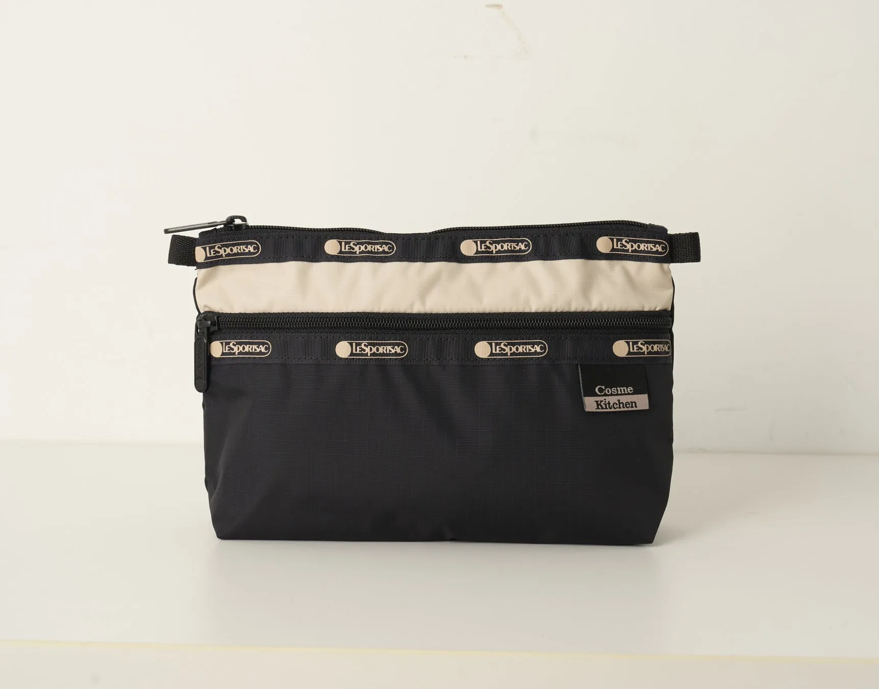 LeSportsacのコスメポーチ。黒とベージュの配色で、前面に3つのファスナーが付いています。ブランドロゴが繰り返し配置されています。