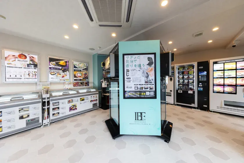 店内には、冷凍食品や香りに関する商品が並んでいる。ポスターや自動販売機も見える。