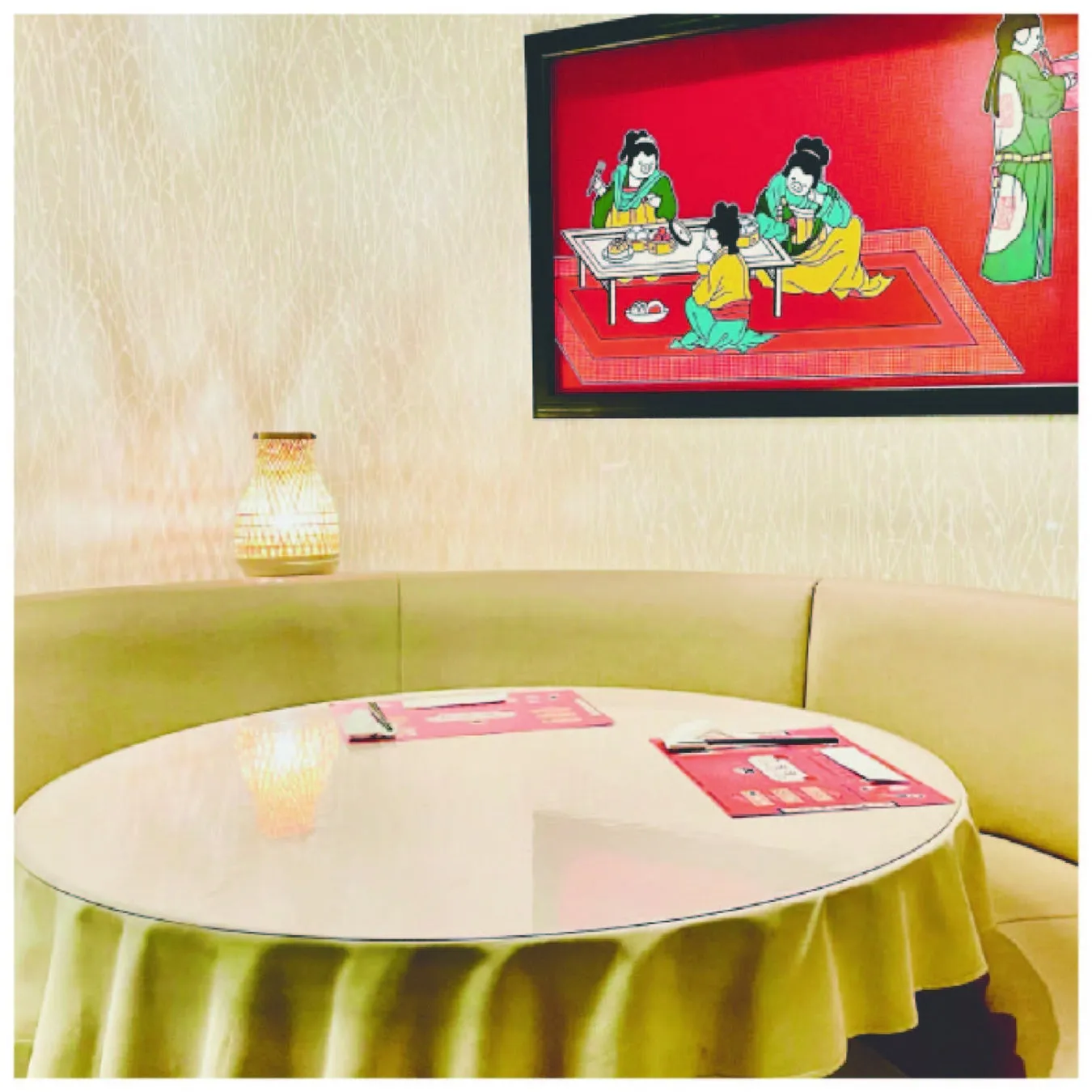 円卓とソファ席のあるレストランの様子。壁には絵画が飾られており、テーブルにはメニューが置かれている。