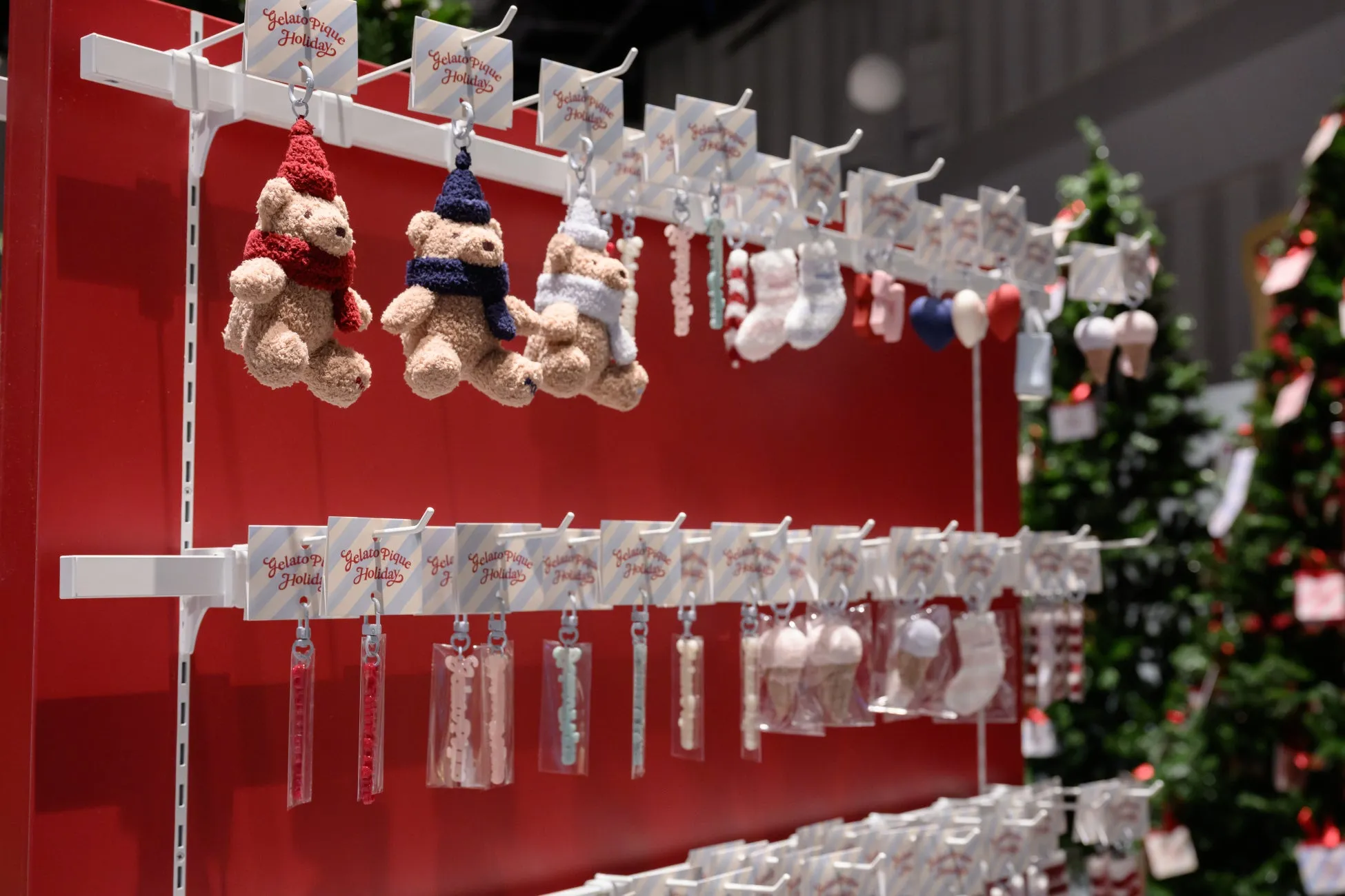 クリスマスシーズンをテーマにした、テディベアのキーホルダーや、お菓子、オーナメントが並んだディスプレイの写真です。「Gelato Pique Holiday」のロゴが入ったタグがついています。