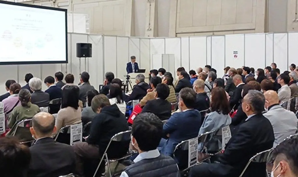 プレゼンテーションをしている様子。多くの人が椅子に座ってプレゼンテーションを聞いている。