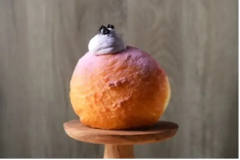 木製の台に載った、グラデーションカラーのパンケーキのようなもの。上にはクリームと、小さな黒い飾りが乗っている。