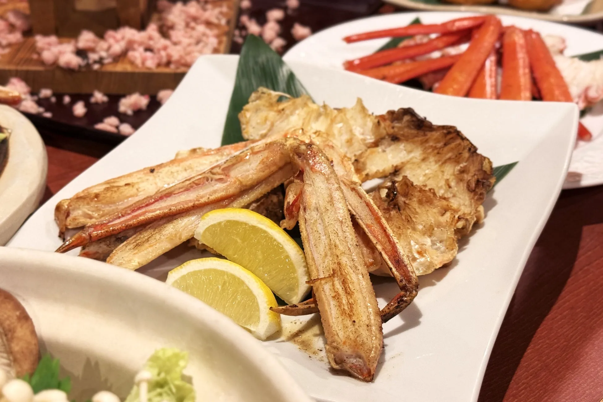 カニ料理の盛り合わせ。焼きガニ、カニの爪、レモンスライスが白皿に盛り付けられている。
