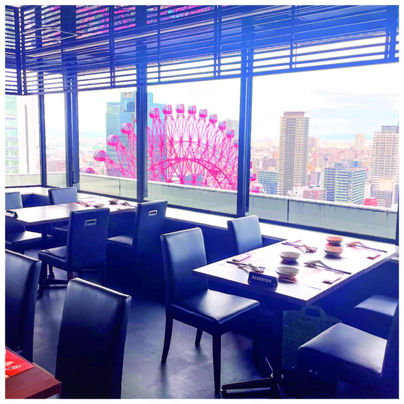 窓から観覧車が見えるレストランの風景。テーブルには食器がセットされ、予約席の札が置かれている。窓の外には街並みも見える。