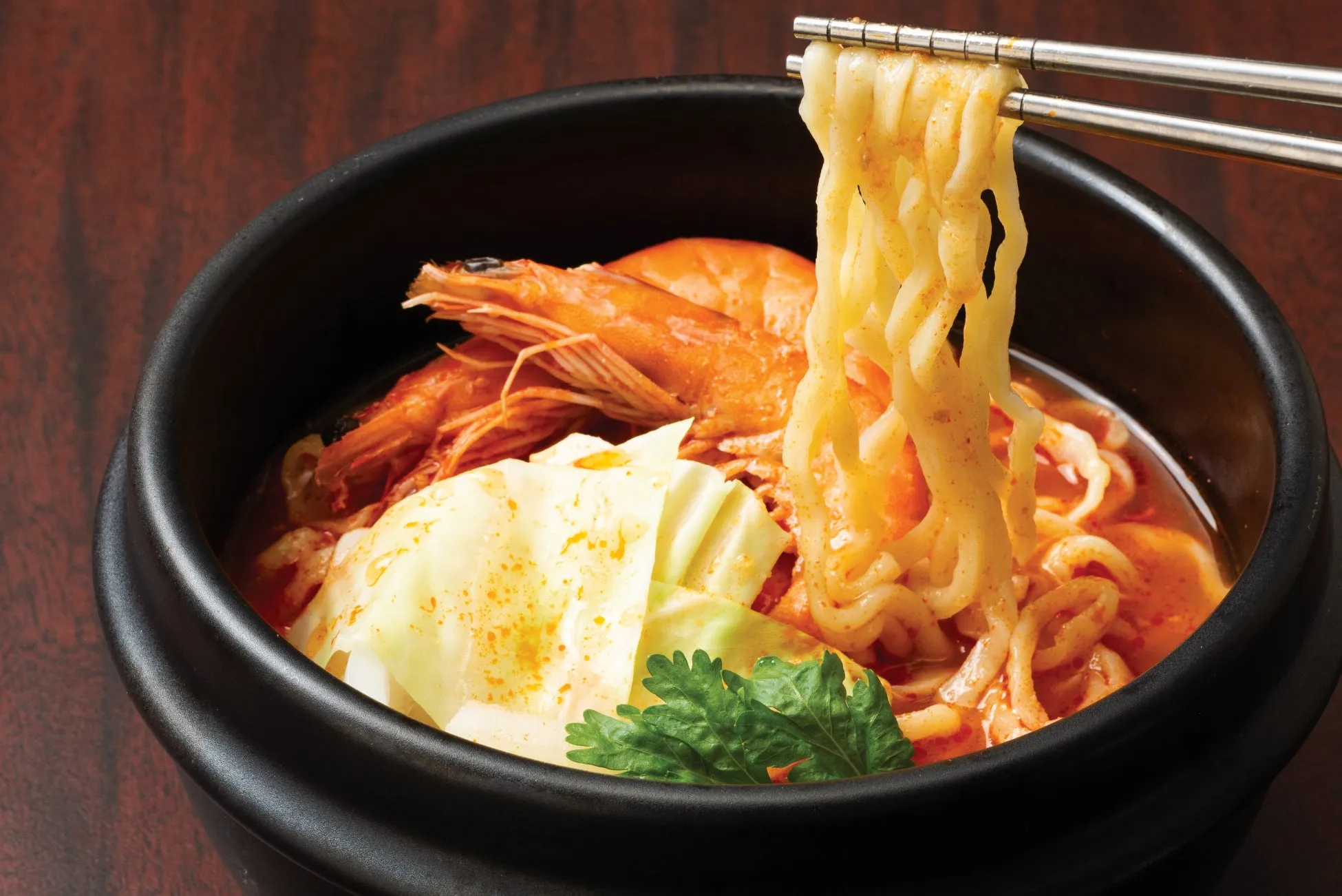 エビと野菜が入ったラーメンのクローズアップ写真。箸で麺を持ち上げている。