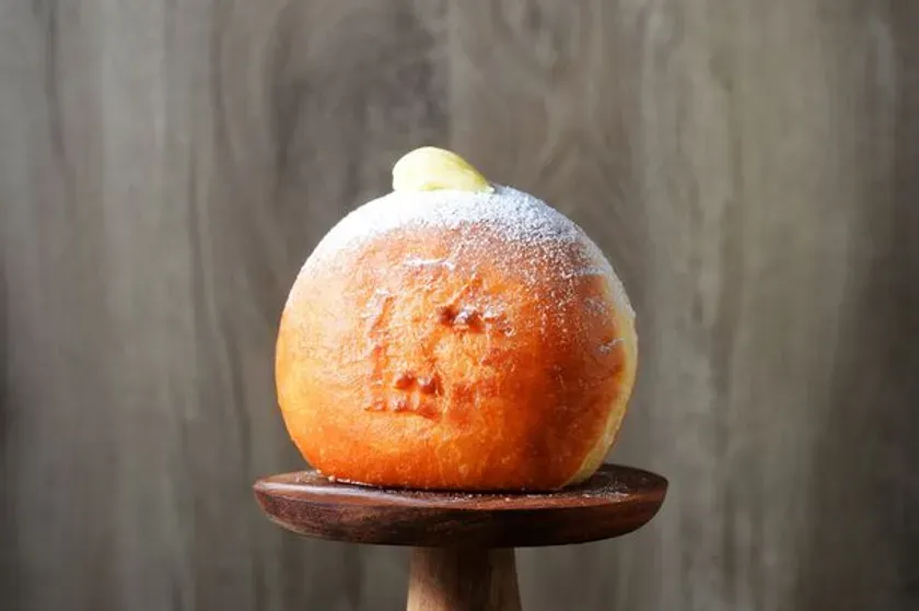 木製の台に載った、粉砂糖がまぶされた丸いパン。上にはホイップクリームが乗っている。