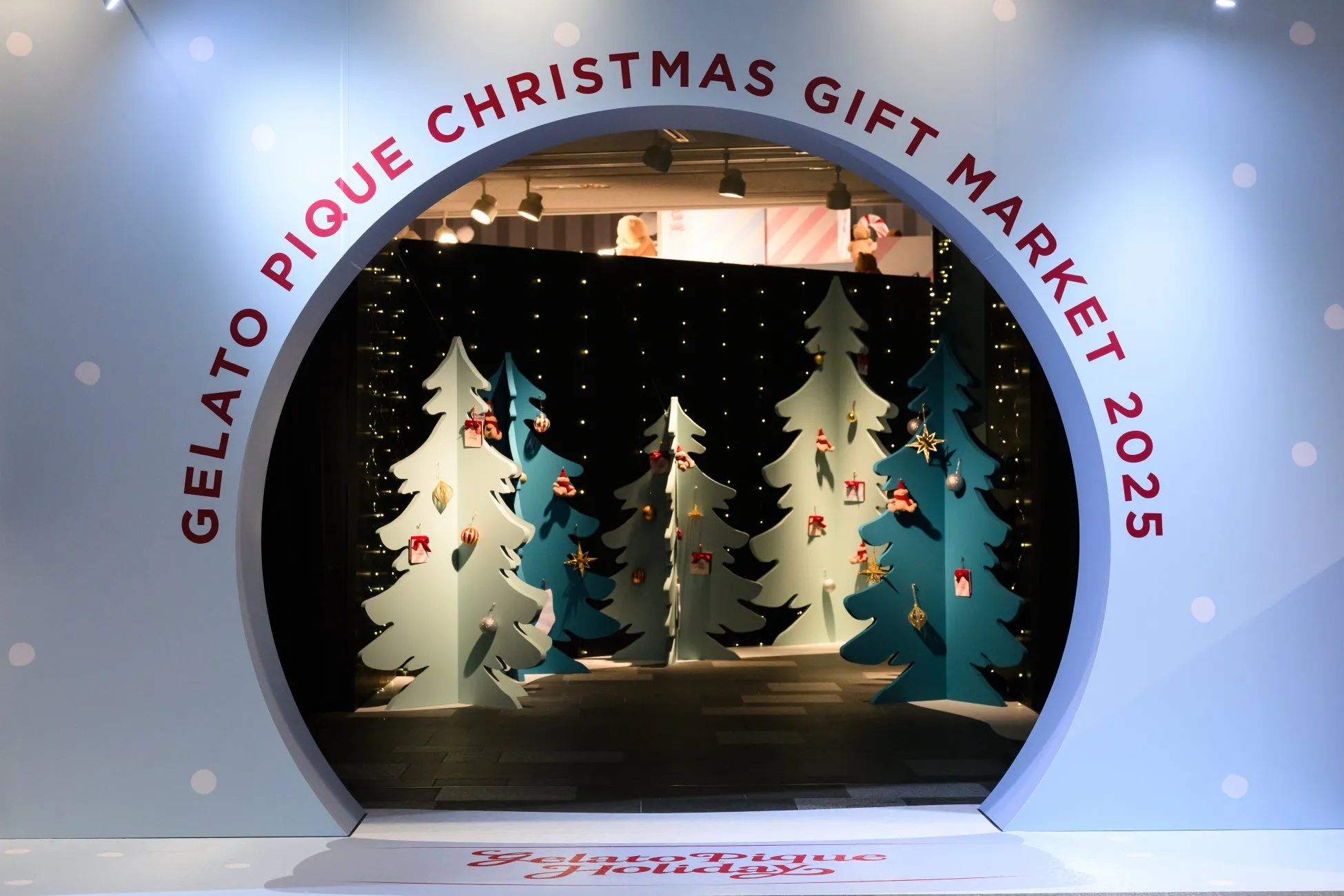 クリスマスをテーマにしたイベントの入り口。ジェラートピケのロゴと、クリスマスギフトマーケットの文字がアーチ状に配置されている。アーチの中には、クリスマスツリーの装飾が施された空間が広がっている。