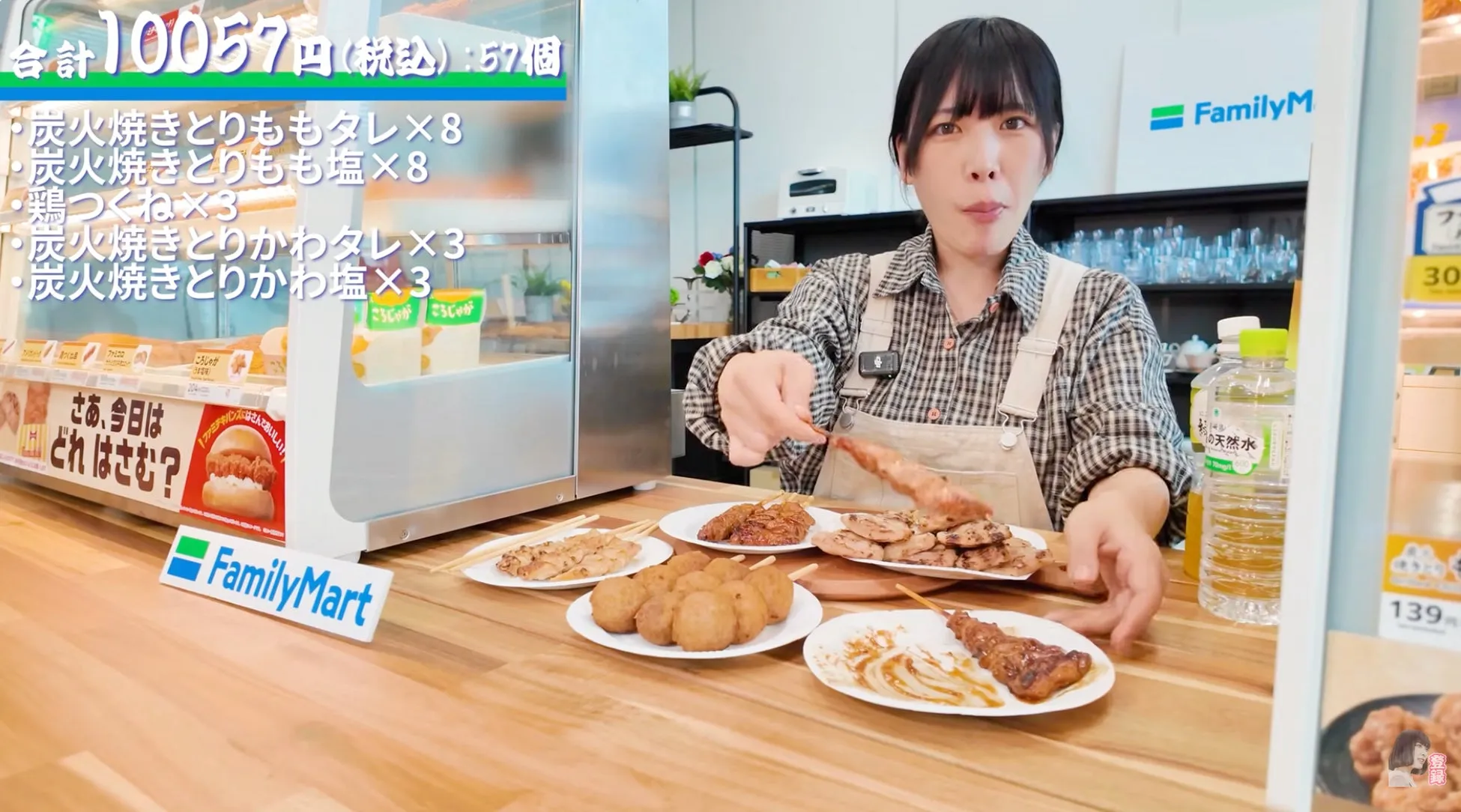 ファミリーマートの焼き鳥や揚げ物を紹介している女性の画像です。様々な種類の焼き鳥と、鶏つくね、ころじゃがなどがテーブルに並べられています。女性は焼き鳥を手に取りながら説明しています。