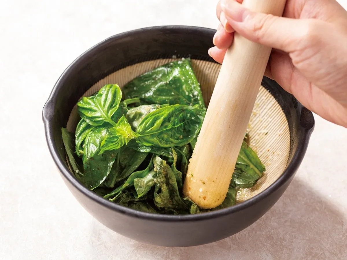 すり鉢の中でバジルをすりこぎで潰している様子