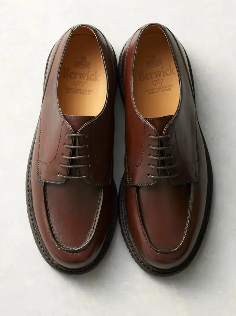 茶色の革靴が2足並んで写っている画像です。革靴は、紐で結ぶタイプで、ブランド名とロゴが靴の内側に印字されています。背景は白いです。