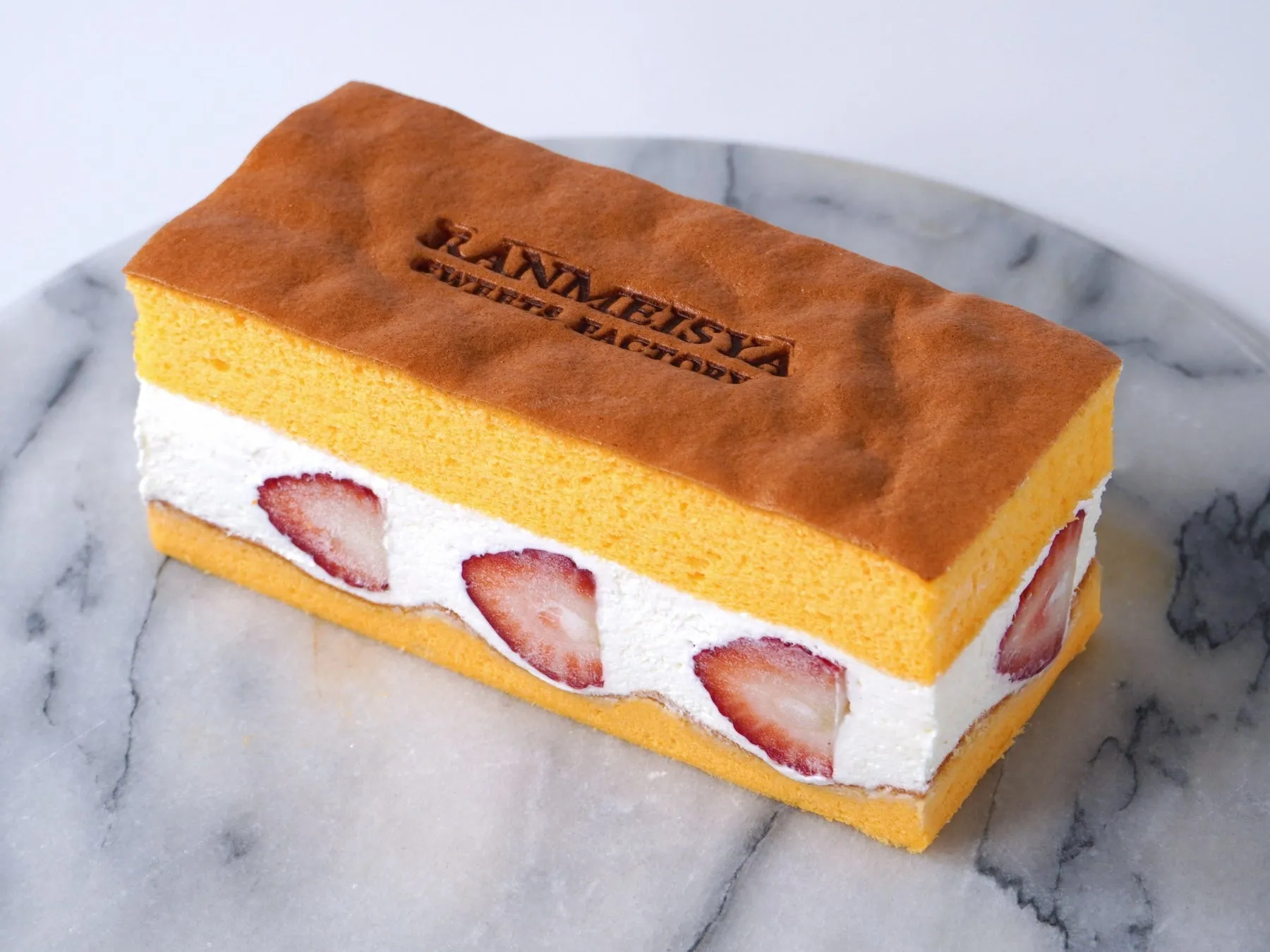スポンジケーキに生クリームとイチゴが挟まれたケーキが、大理石の台に置かれている写真です。