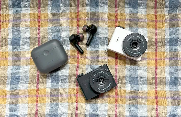 チェック柄の布の上に置かれた、イヤホン、充電ケース、カメラの写真です。
