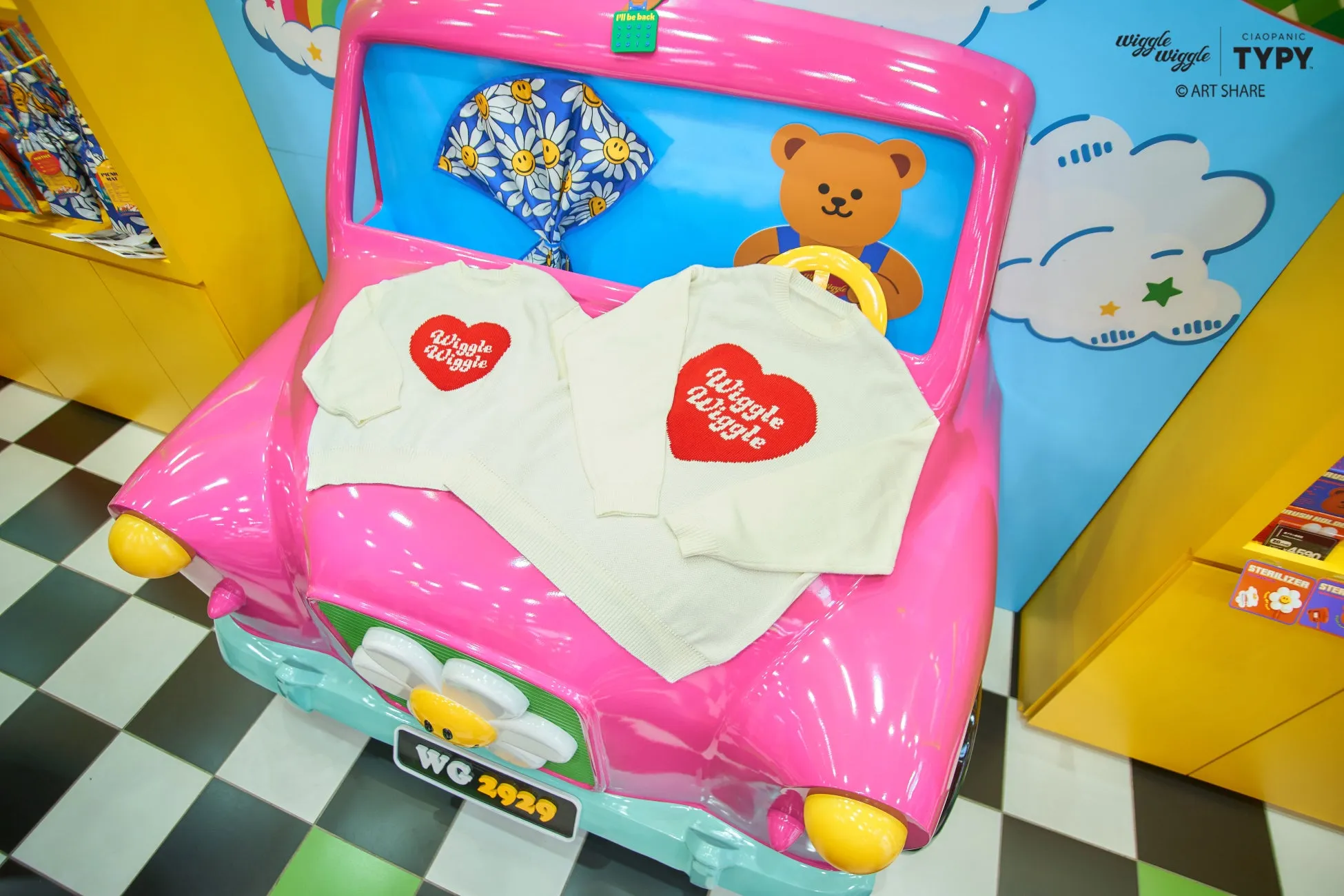 ピンクの車を模したディスプレイに、白いセーターが2枚置かれている。セーターには赤いハートの中に「Wiggle Wiggle」の文字が書かれている。