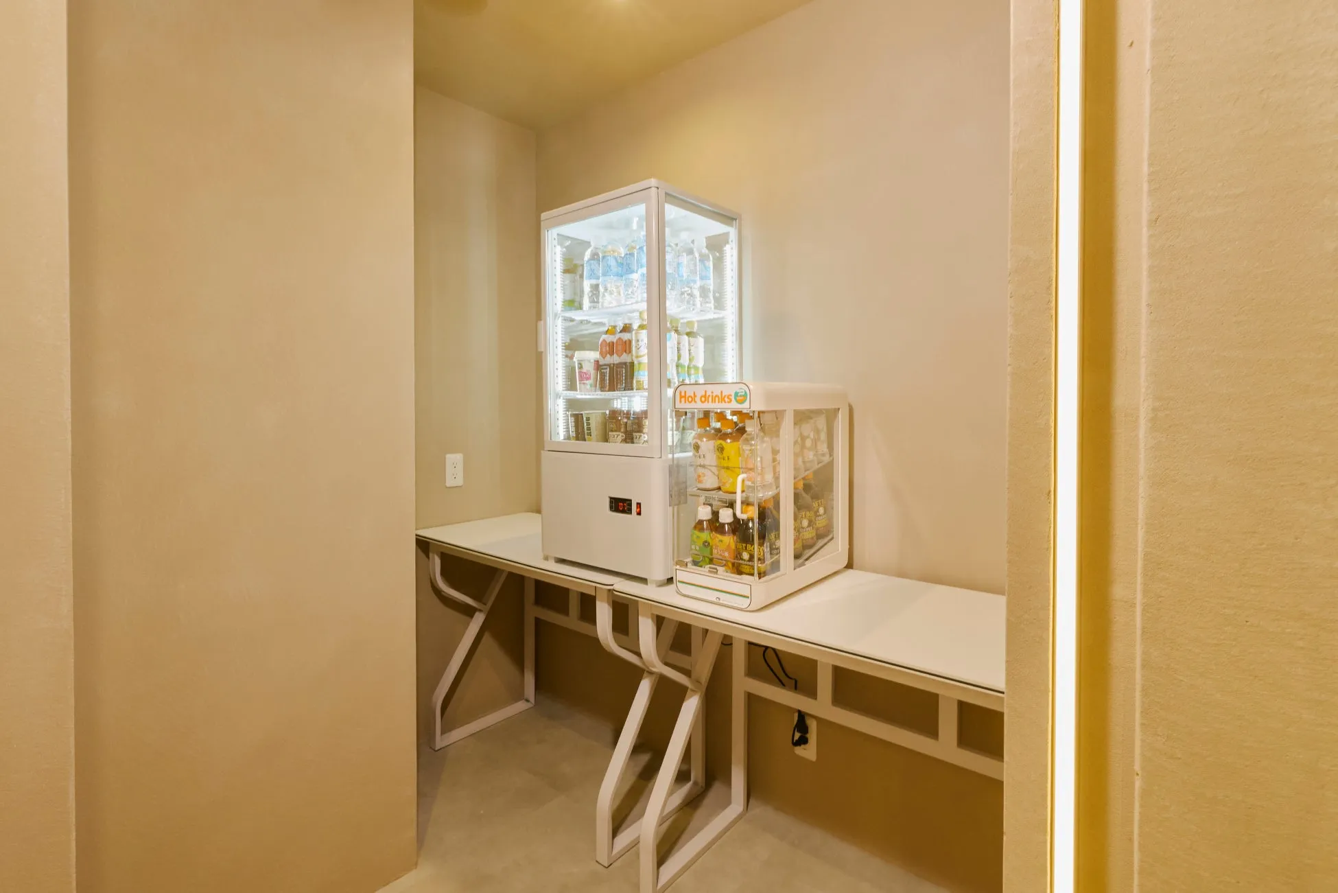 白い冷蔵庫と、飲み物が並んだショーケースが置かれた部屋の写真です。ショーケースには、「Hot drinks」の文字が見えます。