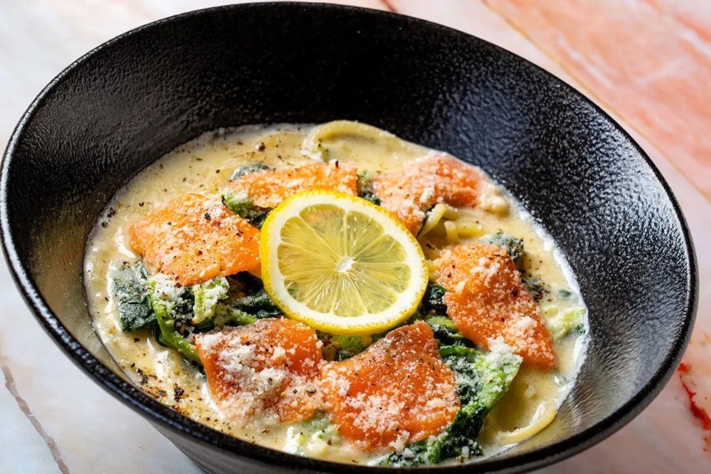 黒い器に入ったサーモンとパスタの料理。レモンスライスが添えられている。