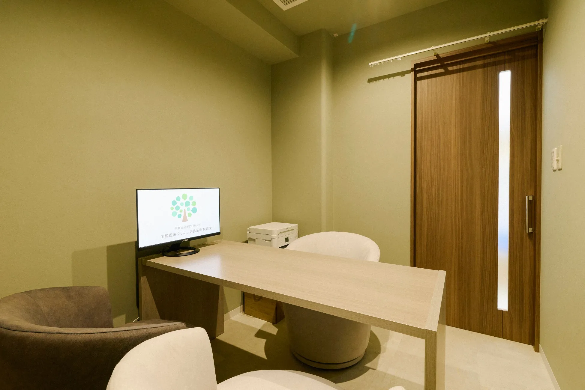 クリニックの診察室の様子。机と椅子、モニター、プリンターなどが配置されており、落ち着いた雰囲気。