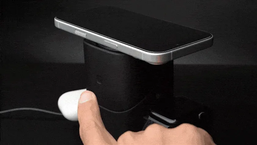 スマートフォン、AirPods、充電器が写った画像です。スマートフォンは充電器の上に置かれており、AirPodsは充電器に接続されています。指がAirPodsに触れています。