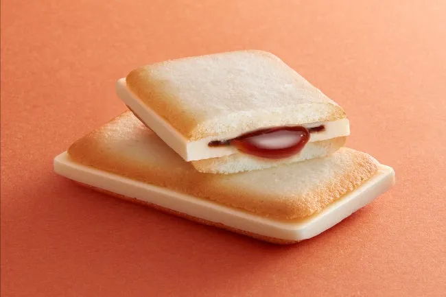 2つの四角いクッキーが積み重なっており、間に赤いソースが入っています。背景はオレンジ色です。