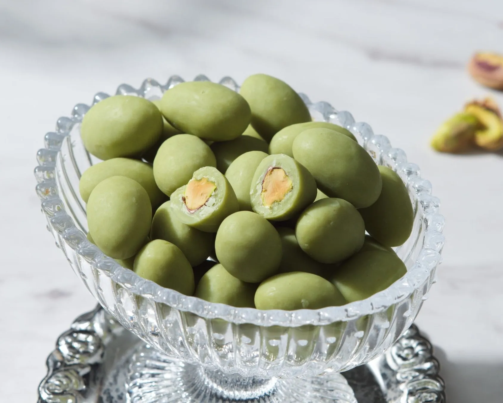 ガラスの器に入ったピスタチオチョコレートの写真です。チョコレートは緑色で、ピスタチオが包まれています。一部は割れており、中のピスタチオが見えています。